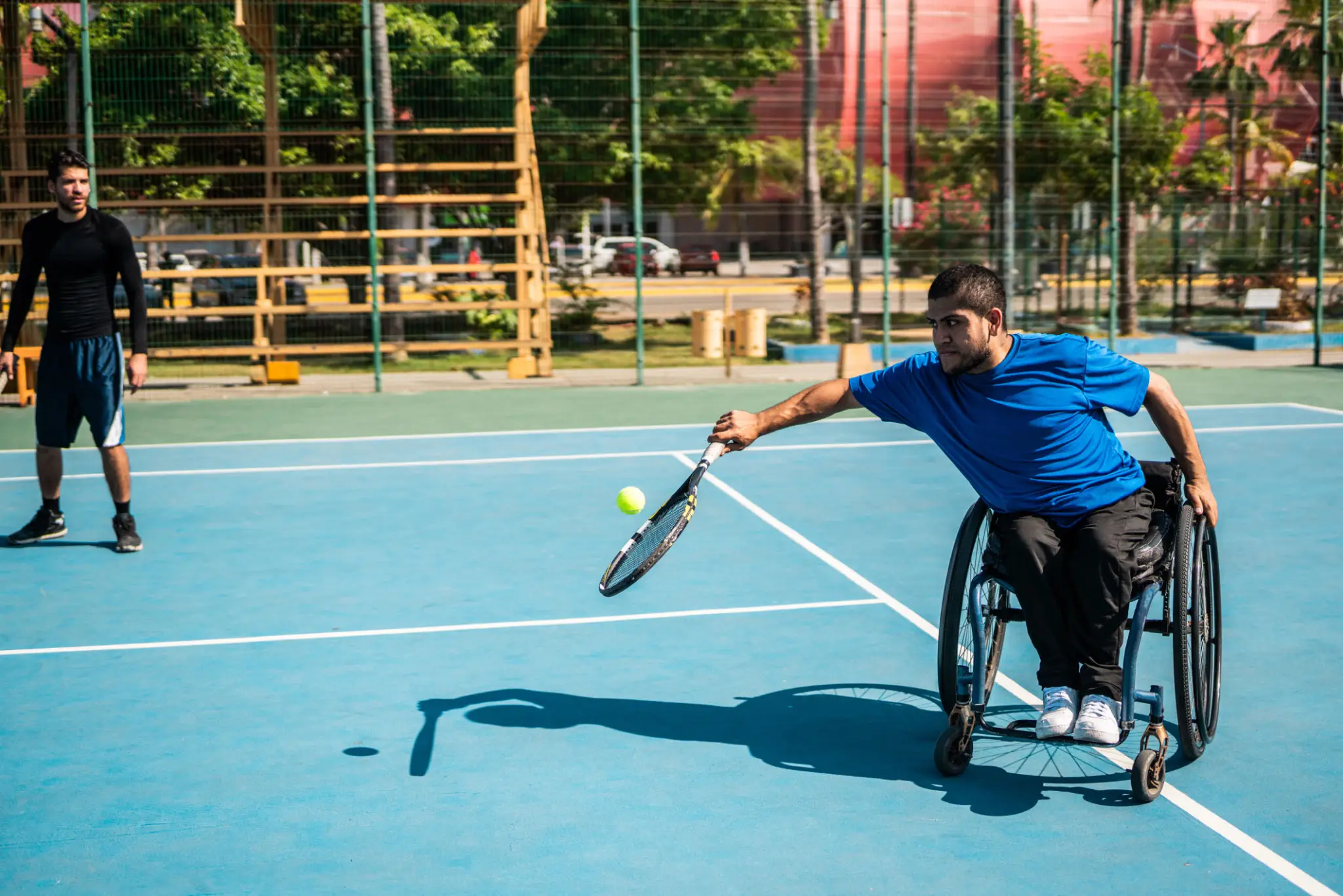 Man in wheelchair playing tennis on an outdoor court.